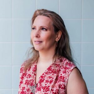 Saskia Wenniger In red, flowered dress in front of blue, tiled background 
